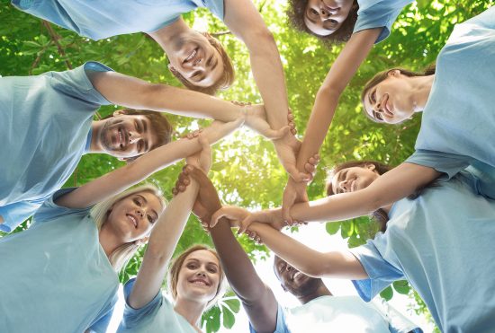 Support concept. Happy volunteers holding hands in circle and smiling, teambuilding exercise, teamwork and help, view from below, copy space