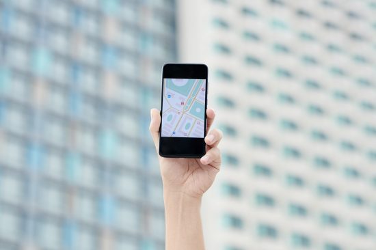 Close-up of male hand holding smartphone with online map on screen against city building